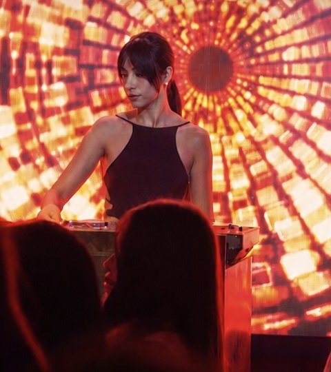 Kamilya performing behind the decks, lit by a radial gold light installation